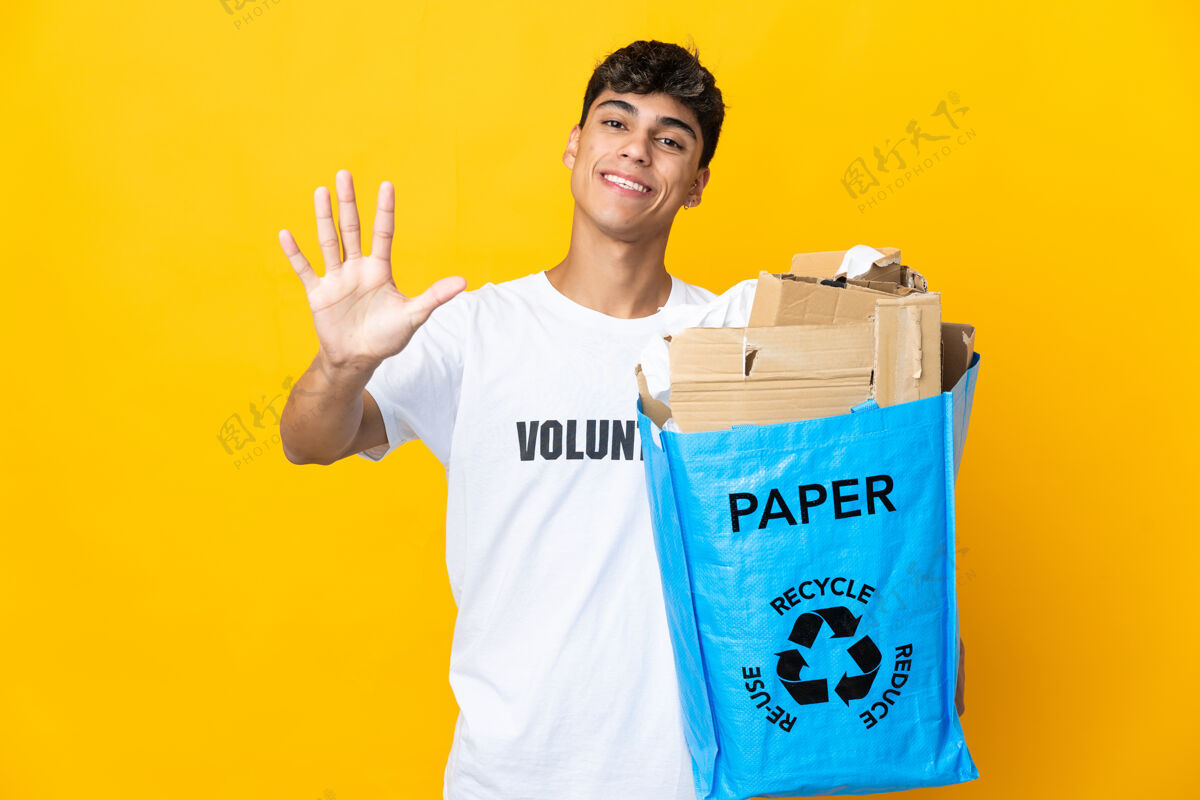 生态系统一个人拿着一个装满纸的回收袋 在隔离的黄色墙壁上用手指数着五个手指保护生态