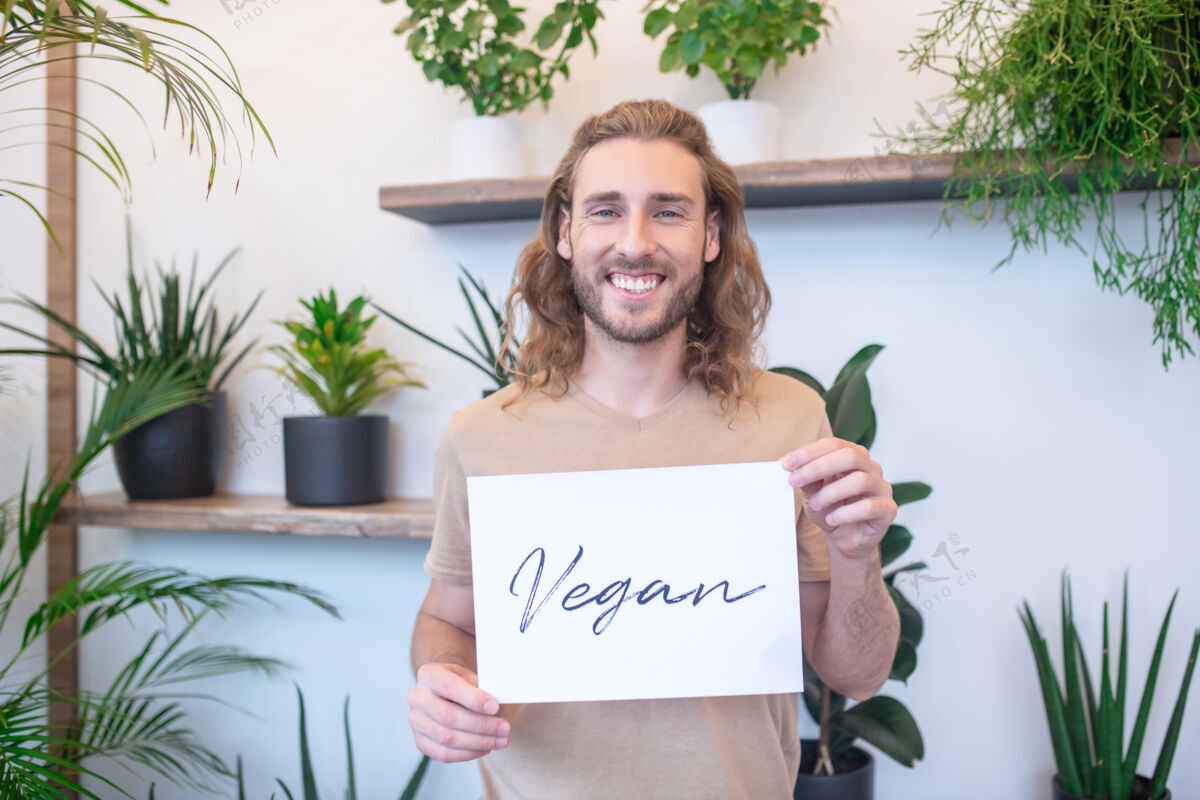 欢乐素食主义者快乐年轻的长毛男人拿着一张写着“素食主义者”的小海报关注素食金发