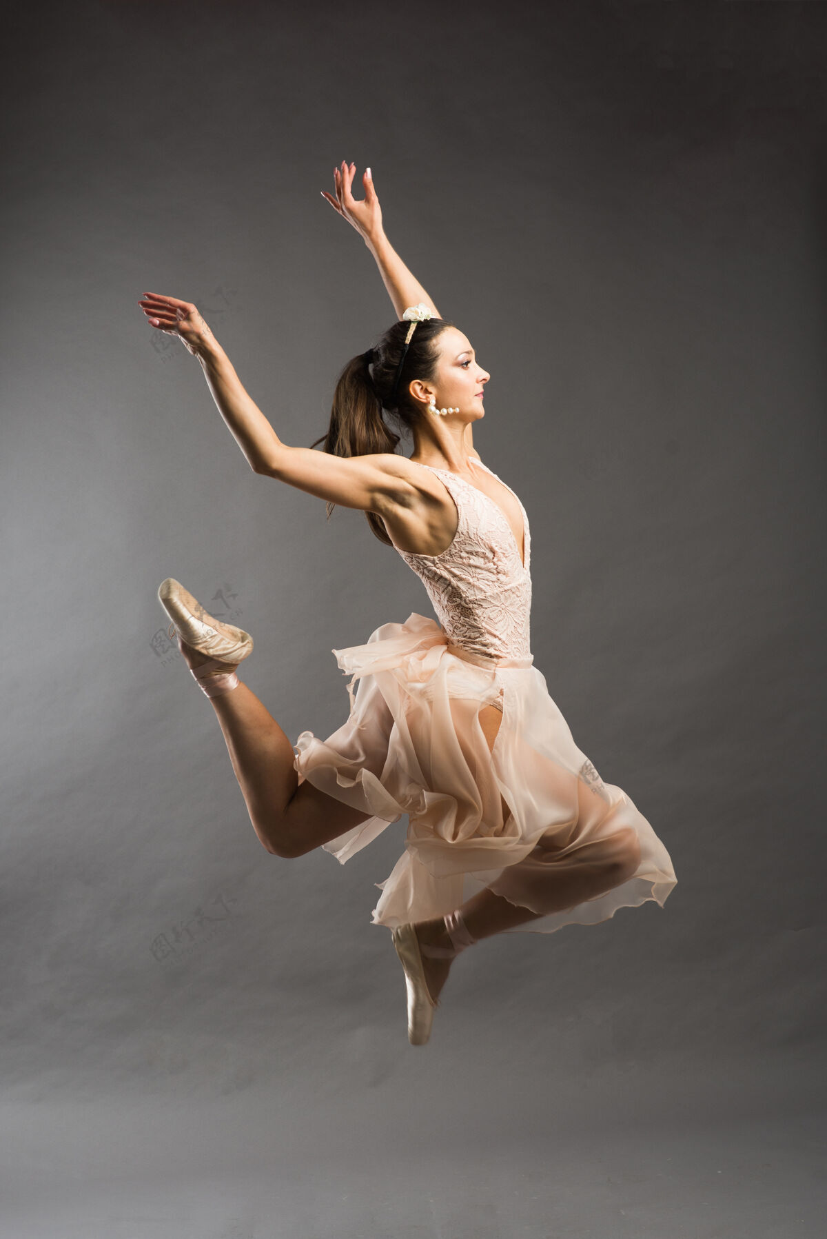 动作年轻漂亮的芭蕾舞演员在浅灰色的工作室背景上穿着米色泳装在尖头上摆姿势颜色拖鞋跳跃