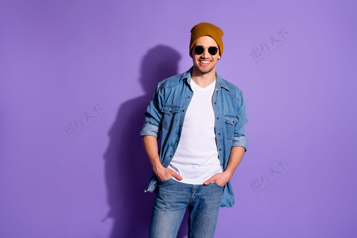 模型照片中 开朗帅气的帅哥双手插在牛仔裤口袋里 微笑着 自信地站在紫色鲜艳的背景下 与世隔绝口袋年轻人衬衫