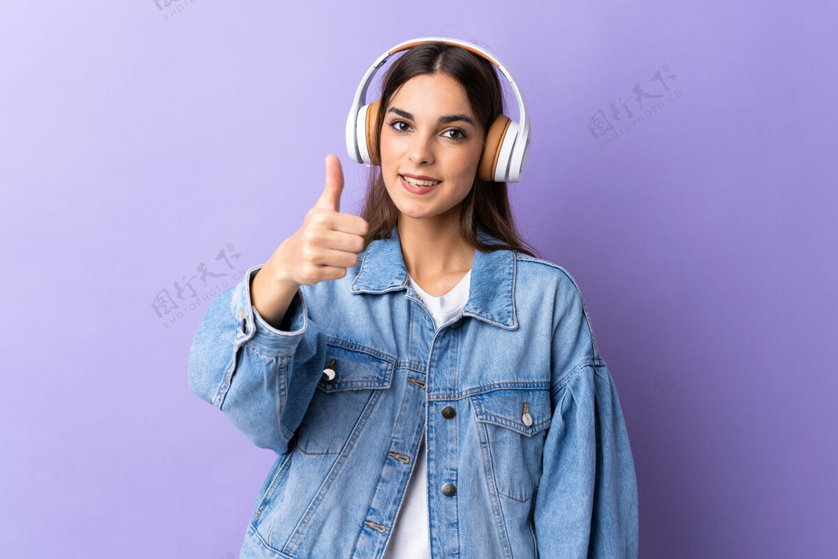 休闲一个年轻的白人妇女被隔离在紫色的背景下 一边听音乐一边竖起大拇指好女人好