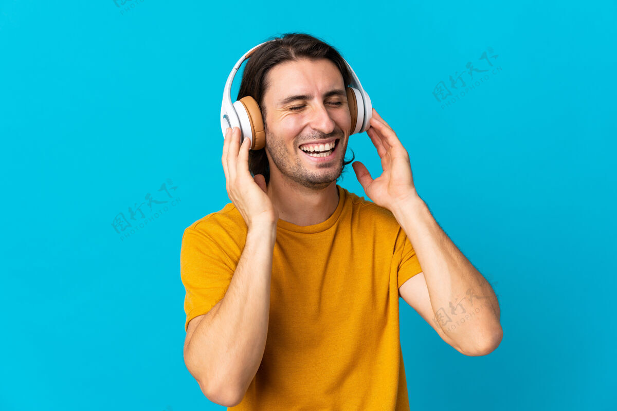 颜色年轻英俊的男人孤零零地站在蓝色的墙上听音乐唱歌音乐家娱乐酷
