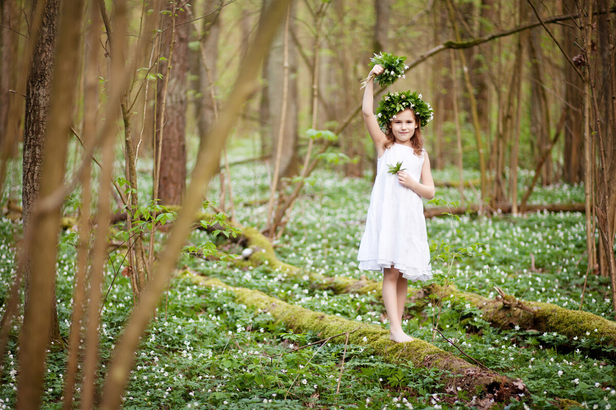 举行穿着白色连衣裙的美丽小女孩在春天的树林里散步一幅美丽小女孩的肖像 头上戴着春天的花环时尚女性快乐