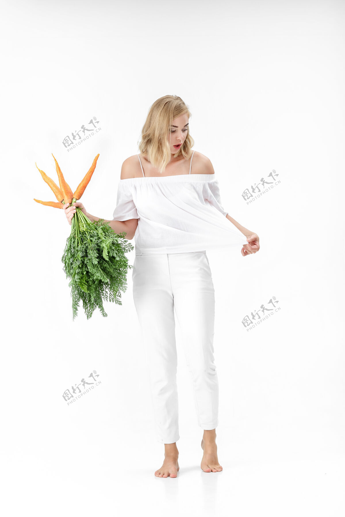蔬菜美丽的金发女人拿着一个新鲜的胡萝卜和绿色的叶子上的白色背景女孩吃胡萝卜会变瘦素食食物背景