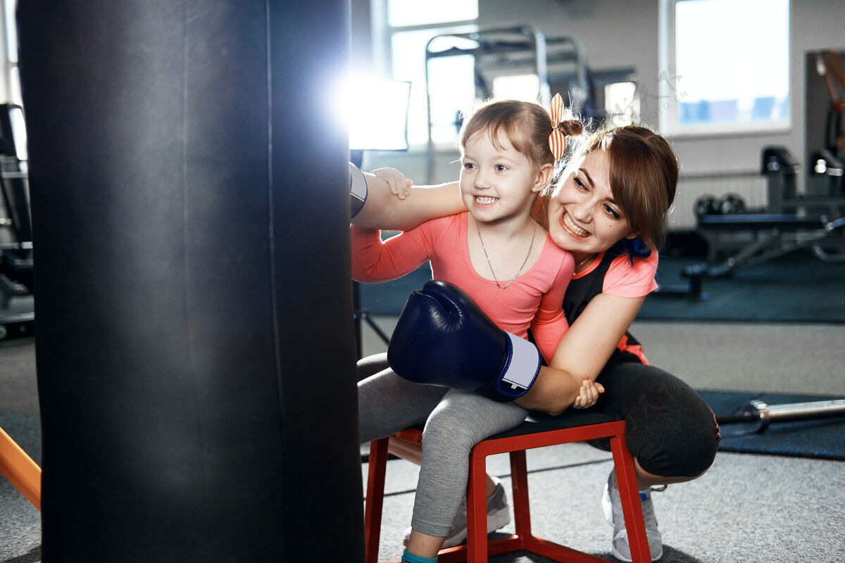 童年小女孩在练习拳击 小女孩教妈妈拳击 有趣的妈妈和女儿在体育馆拳击击球年轻