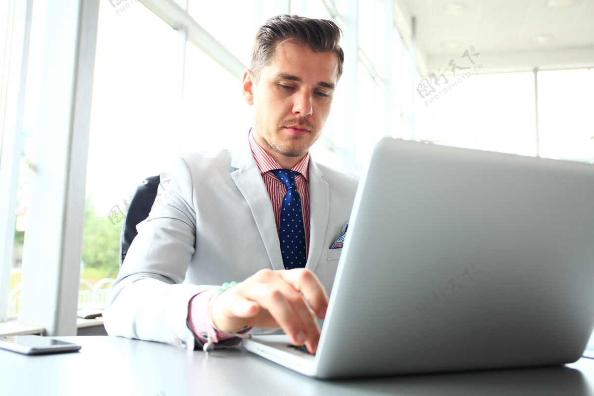 英俊坐在书桌旁的年轻人的画像办公室杨员工在办公室工作时看电脑显示器笔记本电脑办公桌经理