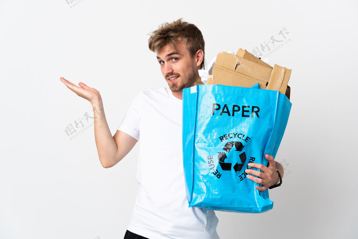 青年年轻的金发男子手里拿着一个装满废纸的回收袋 把回收隔离在白色的手伸到一边 邀请前来人人垃圾