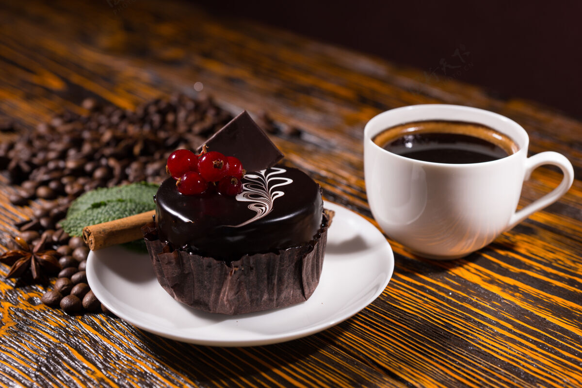 碎片美味的黑巧克力杯蛋糕装饰着红色浆果 白色咖啡杯和木桌上的一堆豆子杯子纸服务
