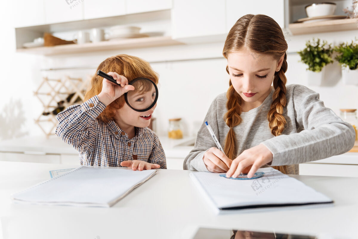 大脑吃一点有趣搞笑活跃的姜男孩玩放大镜 而他的妹妹试图做她的家庭作业的数学课休闲厨房发展
