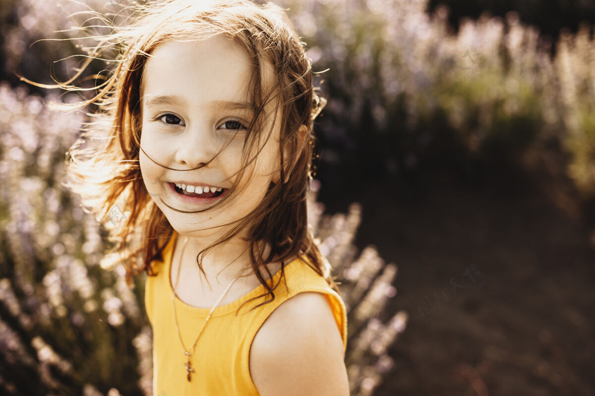 日落一个可爱的小女孩穿着黄色的衣服 在夕阳下的一片花丛中看着相机笑着的画像女孩乐趣环境