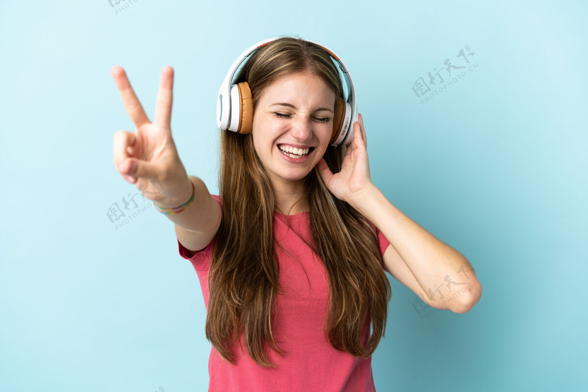 听力年轻的白种女人在蓝色背景下孤独地听音乐和唱歌女人年轻人肖像