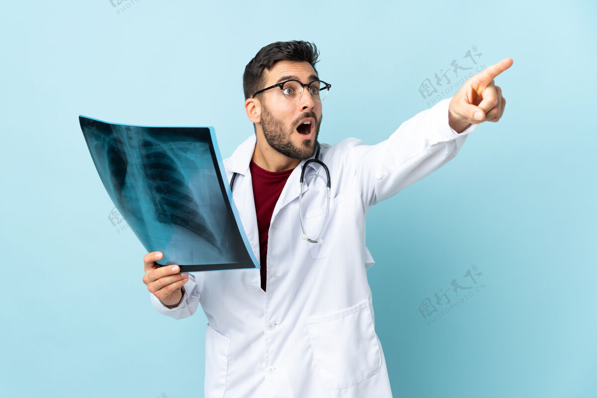 注意专业的创伤医生拿着隔离在蓝色背景上的X光片指着别处男人惊讶医院