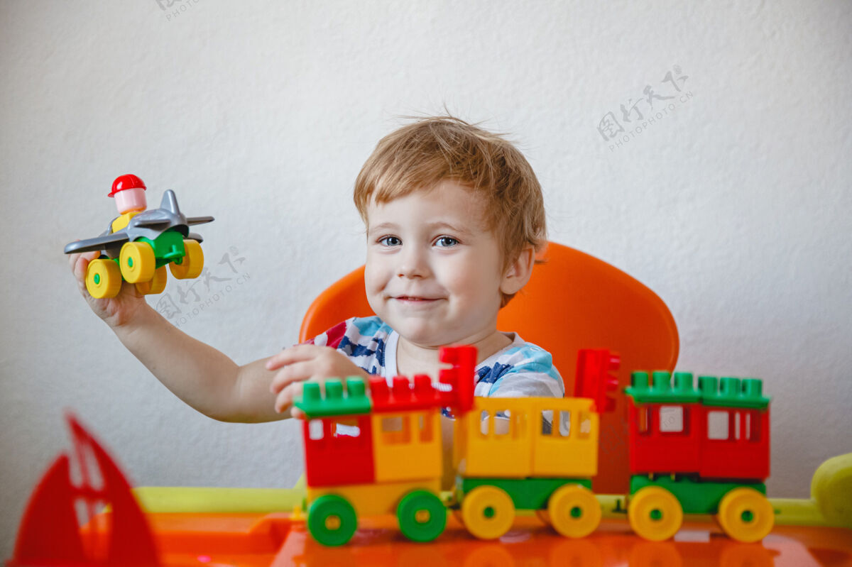 乐趣一个金发小男孩坐在家里一张橙色的儿童桌旁 玩着五颜六色的塑料玩具套件高高质量的照片休闲活动欢呼婴儿期
