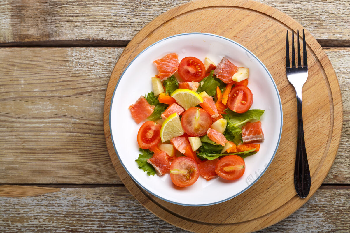 清淡的菜肴一盘三文鱼 樱桃西红柿沙拉和蔬菜沙拉放在一张木桌上 放在叉子旁边的木架上健康鱼片三文鱼