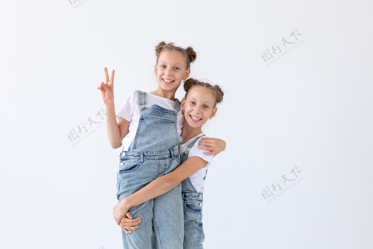 漂亮家庭和爱的概念-两个微笑的双胞胎姐妹拥抱在白色的表面活跃享受快乐
