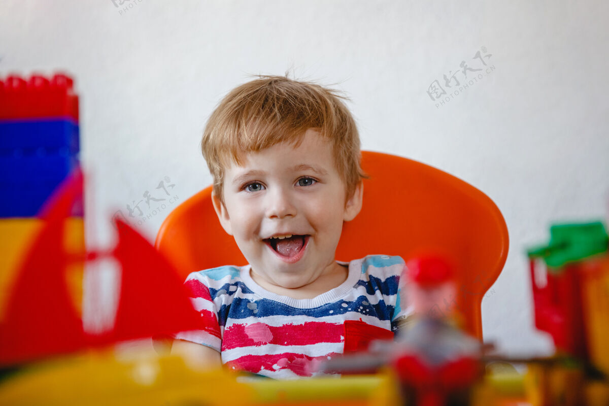欢笑一个金发的笑着的小男孩在鲜艳的塑料中的肖像玩具高高质量的照片欢呼幼儿园婴儿