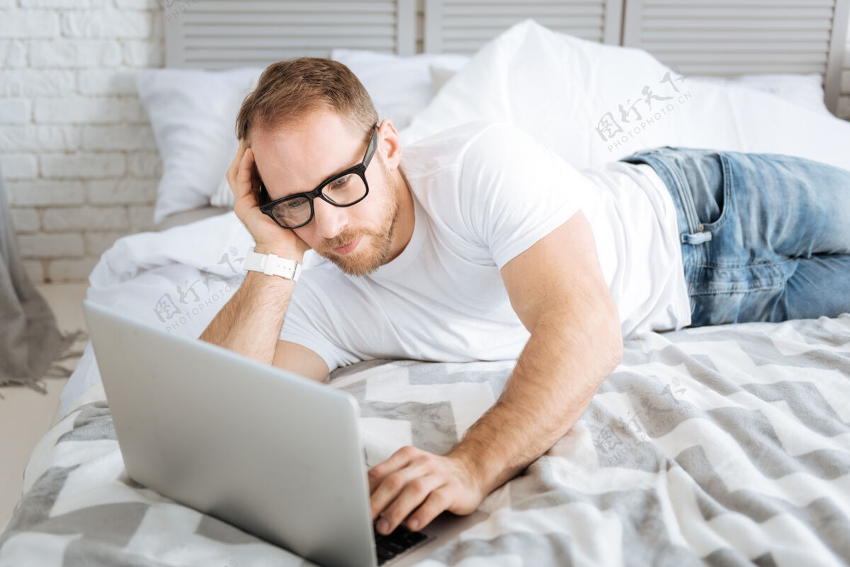 当代做我的自由职业者工作魅力运动迷人的男子躺在床上 使用笔记本电脑 同时表达兴趣和上网内部信息积极性