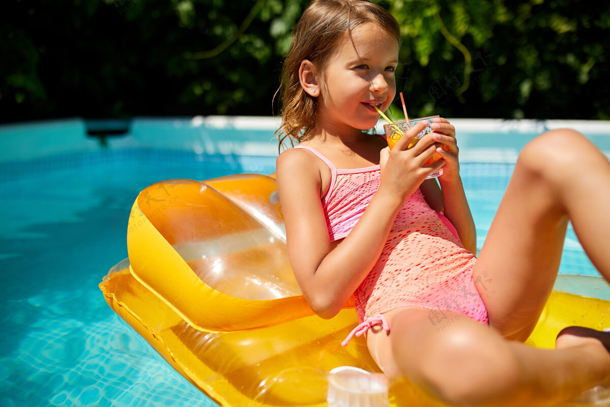美丽小女孩在游泳池里放松 享受日光浴 在家庭度假时在水里的黄色充气床垫上喝果汁玩耍娱乐鸡尾酒