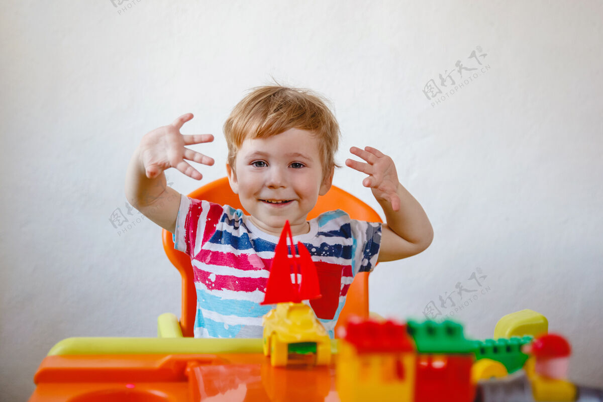 活动一个欢笑的小男孩坐在桌子旁 手里拿着五颜六色的玩具向上向上高质量的照片细节创意欢笑