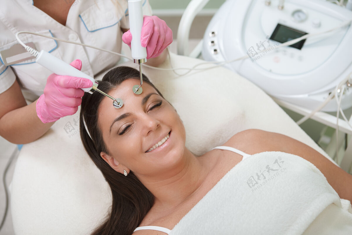 专业在美容院接受护肤治疗时 快乐美丽的大号女人微笑着清洁皮肤护理面部