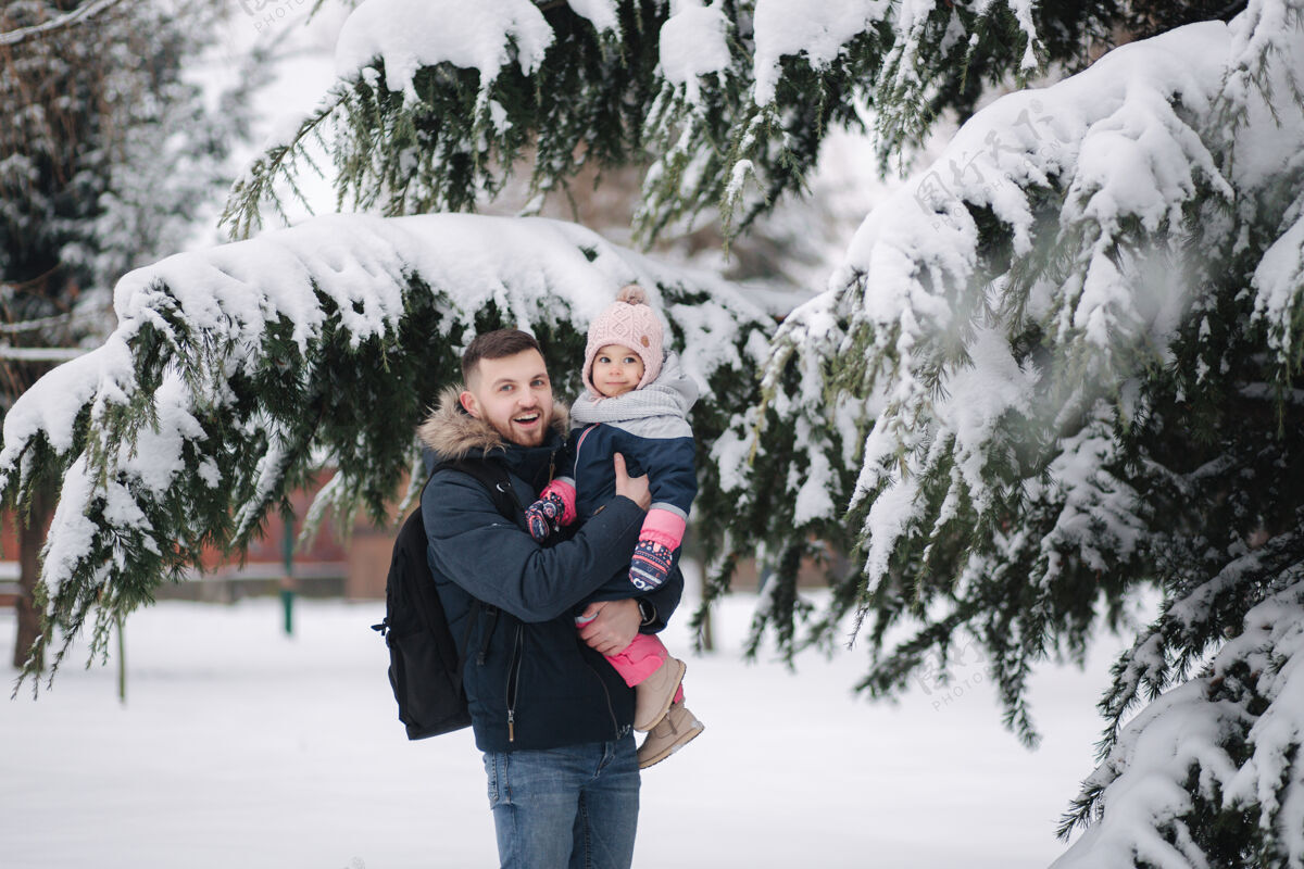 微笑可爱的小女儿和她可爱的爸爸站在雪树旁一起滑梯季节