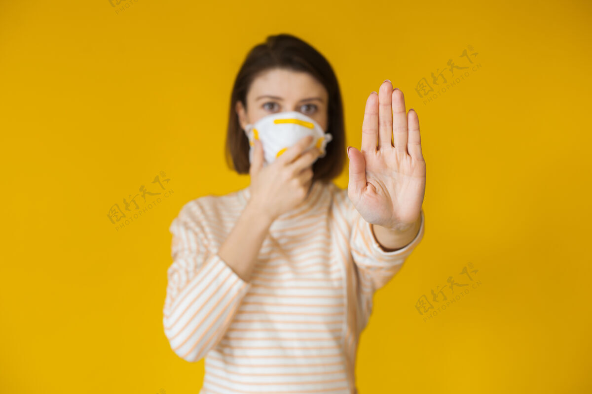 空气一个戴着白色面具的白种女人在黄色的墙上摆姿势 示意停车标志暴发新颖担心