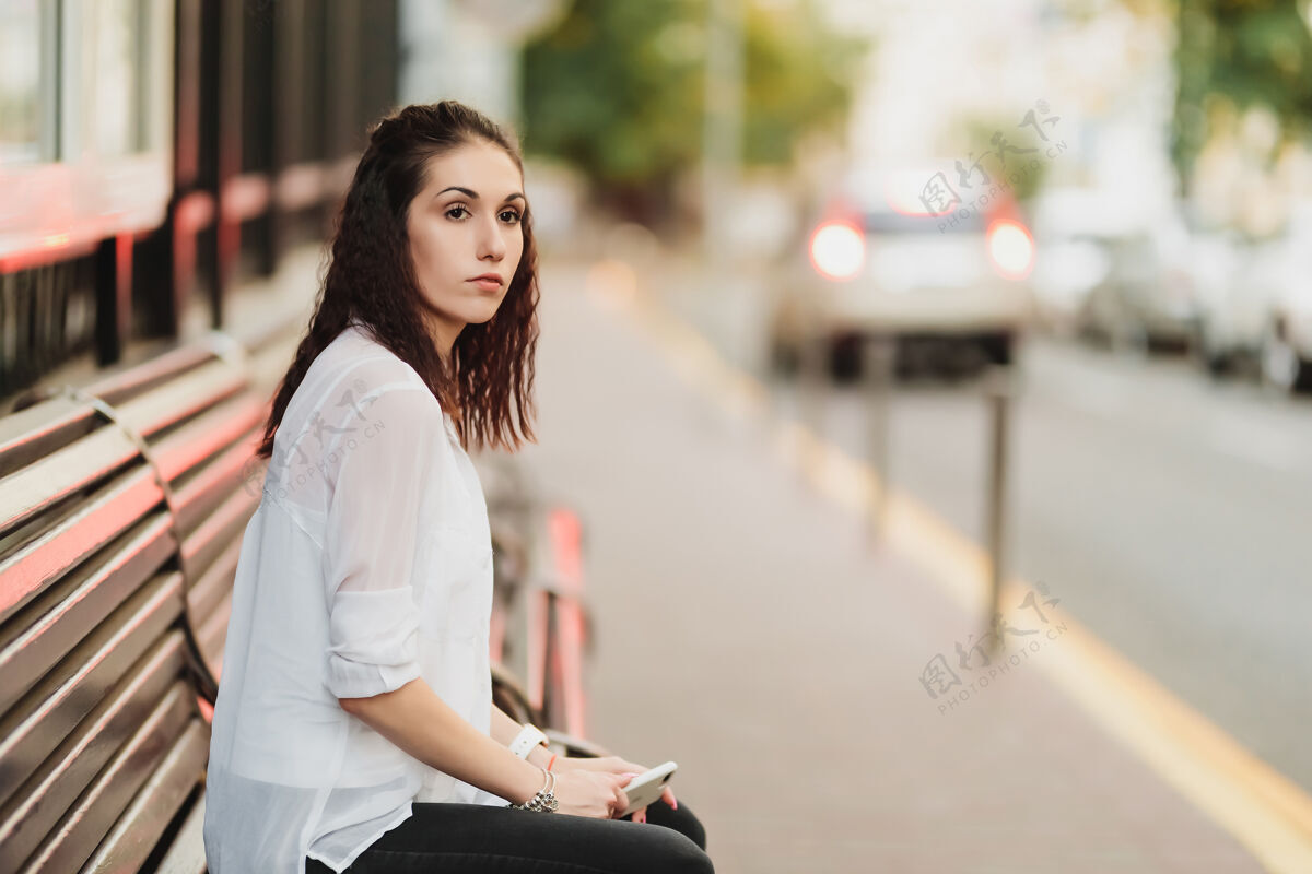 女商人年轻漂亮的女人在车站等公共汽车停高高质量的照片白天公共汽车站城市
