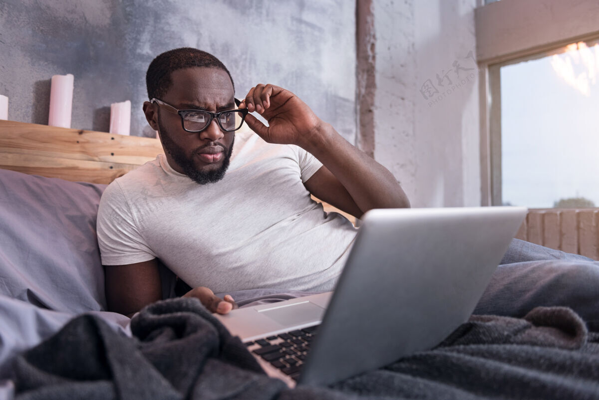 英俊卧室工作非洲年轻人戴着眼镜 躺在床上使用笔记本电脑国际家庭谎言