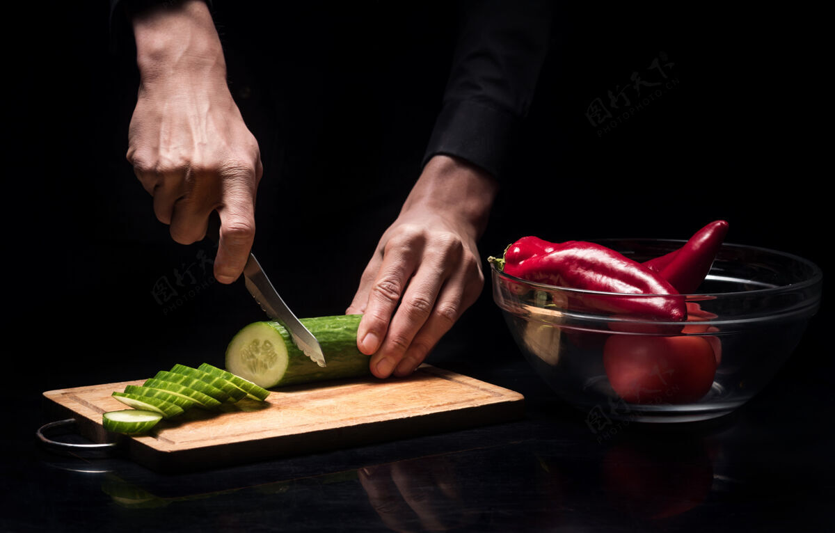 美味多汁的健康接近年轻的厨师手切新鲜蔬菜 同时用黄瓜和甜椒在餐厅做饭菜肴准备自然