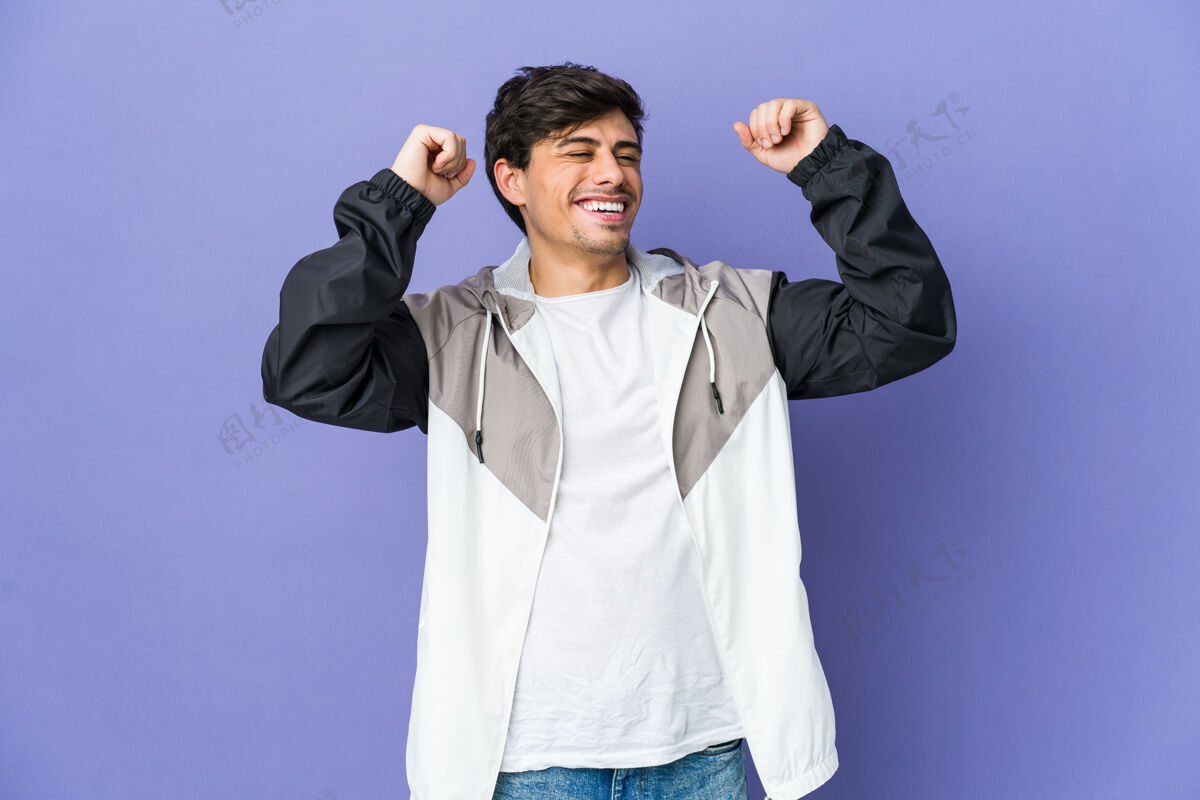 庆祝年轻的酷男人庆祝一个特殊的日子 跳起来 举起双臂与能量表情提高微笑