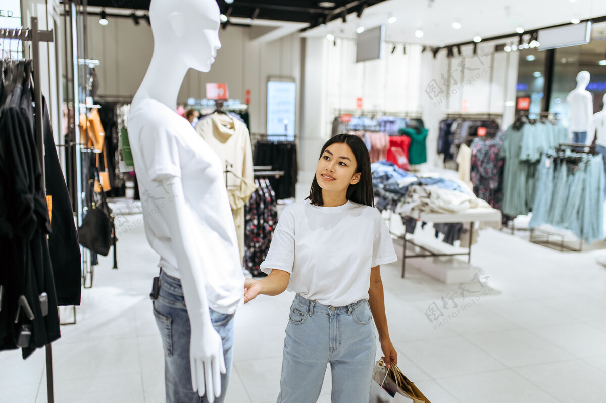 消费主义快乐的女人站在人体模特面前 穿着衣服女店员在时装精品店购物的人 购物狂 看服装的购物者购物者女孩选择