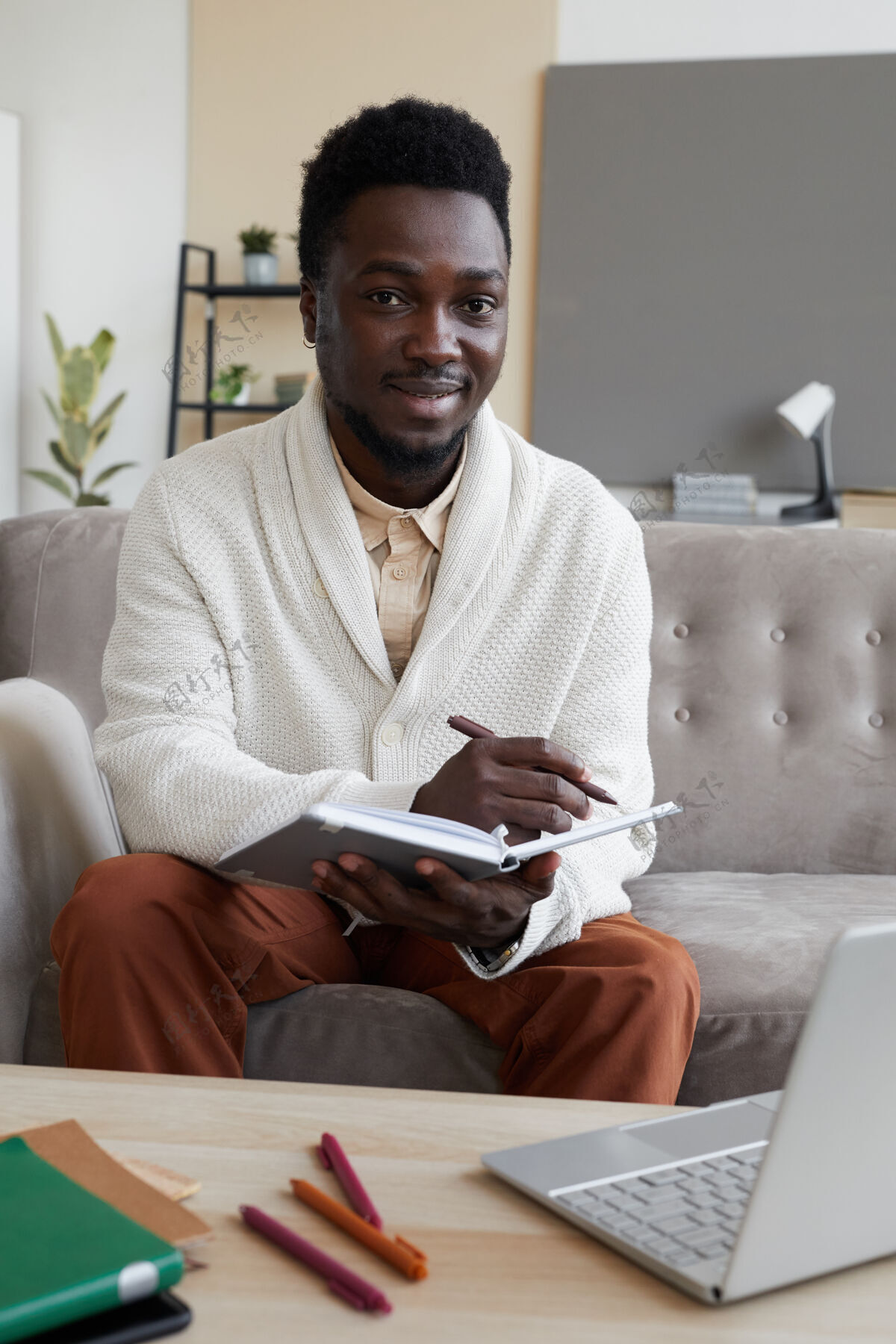 桌子一幅年轻人坐在沙发上 拿着他在家学习的书 面带微笑的画像工作现代技术