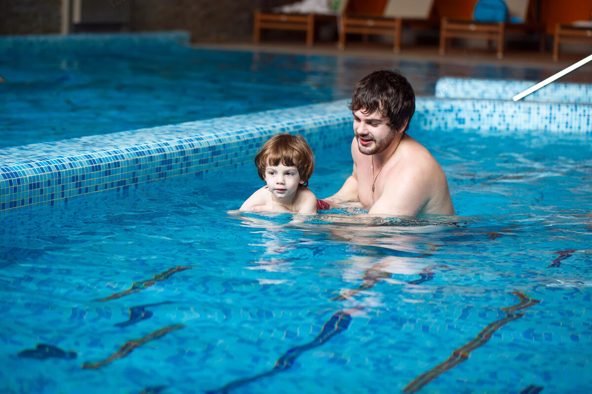男人爸爸教儿子在游泳池里游泳人小乐趣