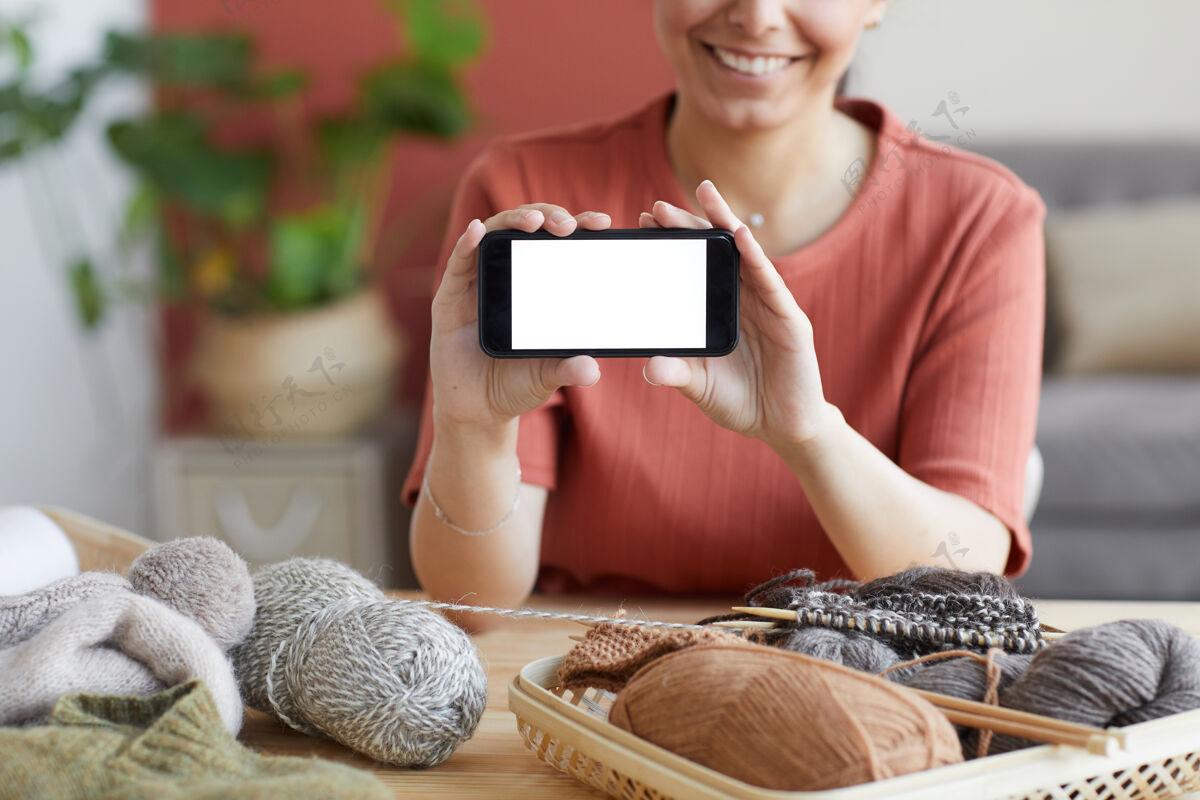 技术坐在桌边毛线中间的年轻女子的特写镜头 展示她的手机的空屏幕分享移动显示