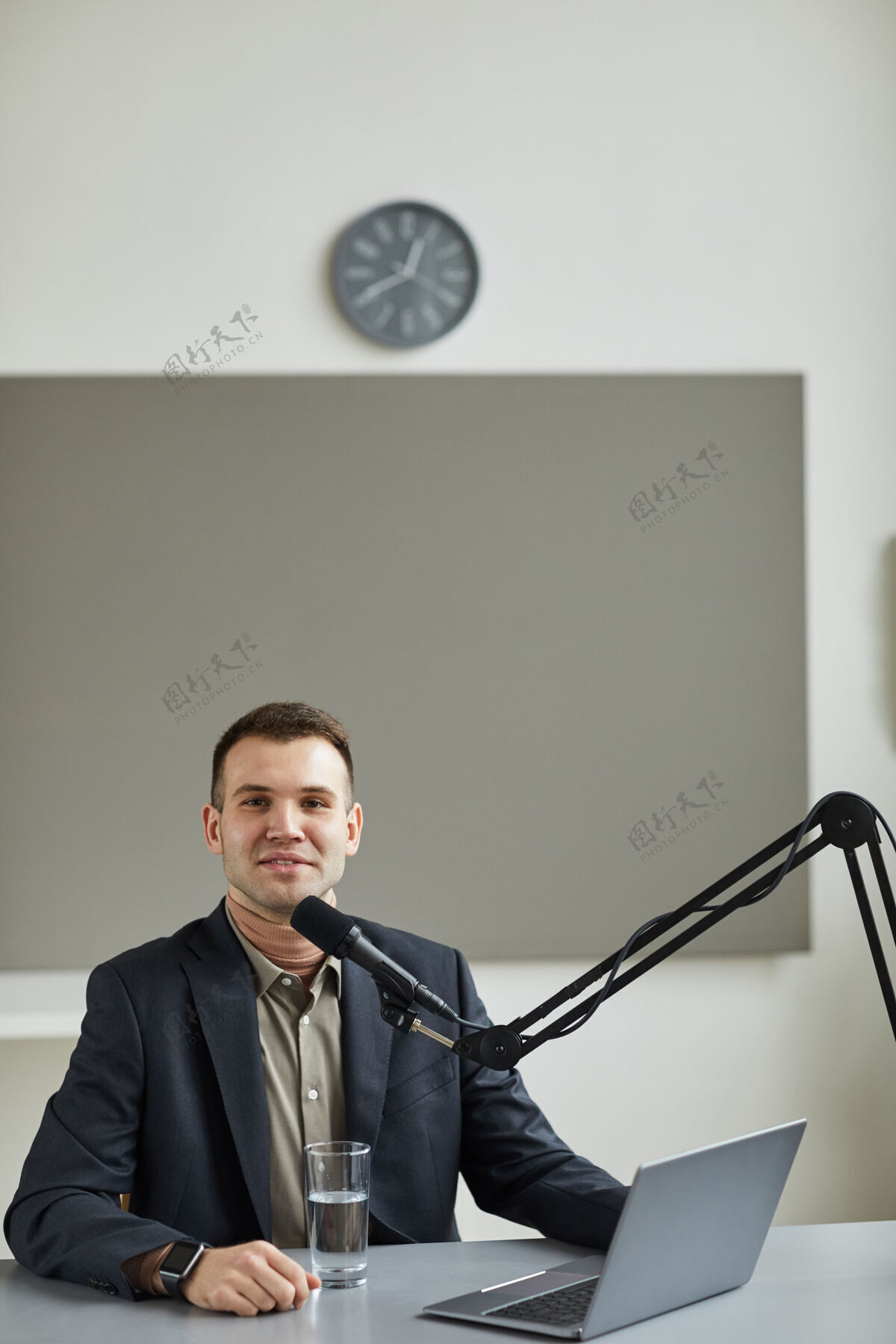 主持年轻的电台主持人微笑在前面的肖像 而发言麦克风在桌上与笔记本电脑职业职业欢呼