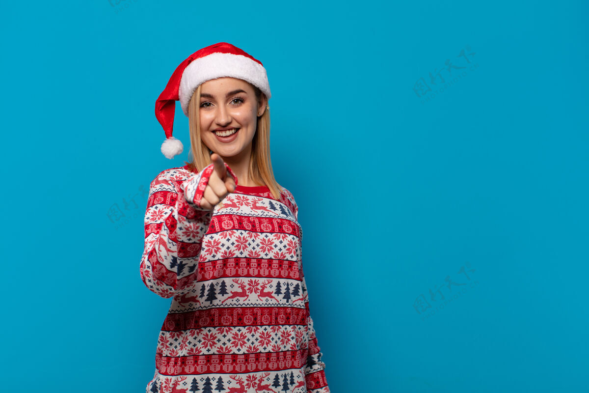漂亮一个戴着圣诞帽的金发女人满意地 自信地指着镜头信心选择美丽