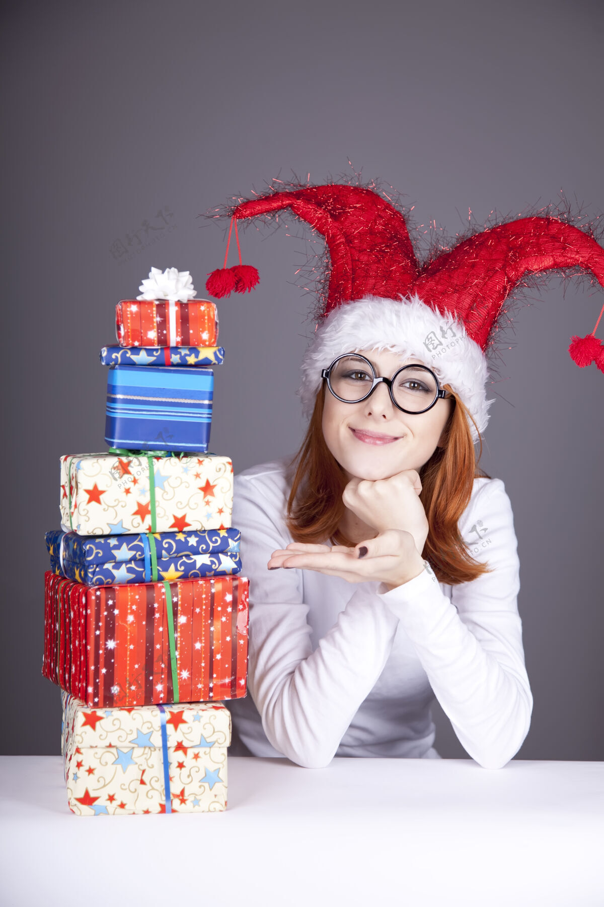 礼物滑稽的红发女孩戴着圣诞帽 戴着带礼盒的眼镜女士桌子欢乐
