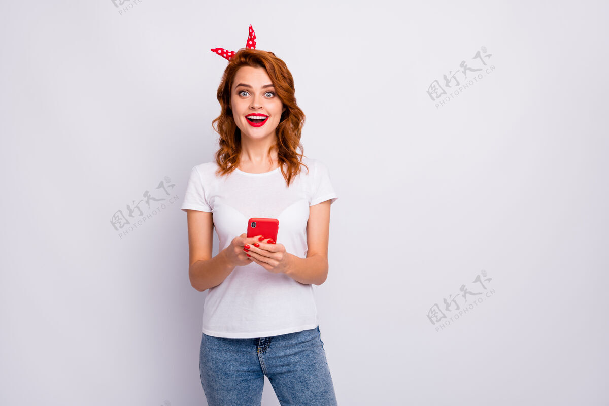 手机兴奋的疯狂女孩的画像使用智能手机阅读社交媒体新闻印象深刻尖叫哇omg穿着时尚的衣服隔着白色的墙信息在线聪明