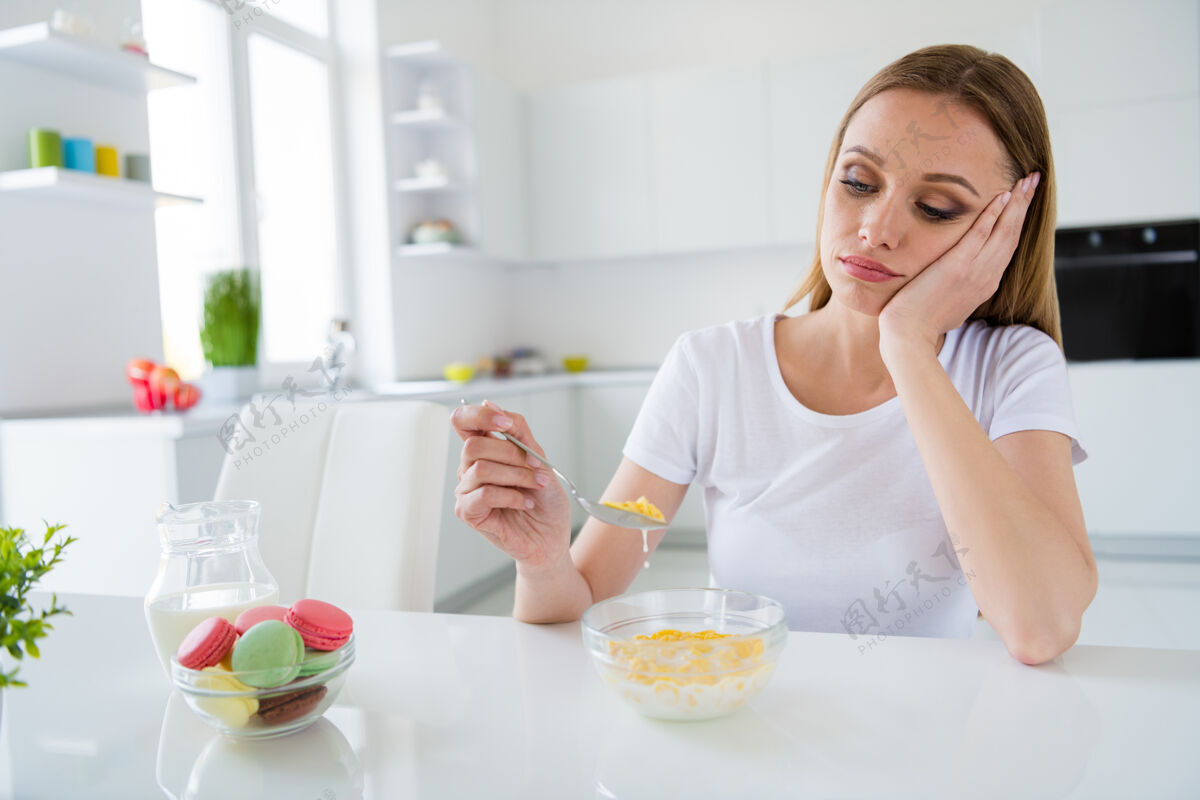 谷类食品照片中相当心烦的主妇拿着勺子不想吃牛奶早餐玉米片厌倦节食无聊的餐桌白光厨房室内无聊早餐膳食