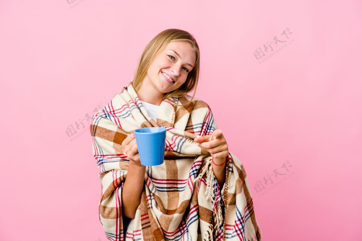 咖啡年轻的俄罗斯女子裹着毯子喝着咖啡欢快地笑着指着前面温暖沙发房子