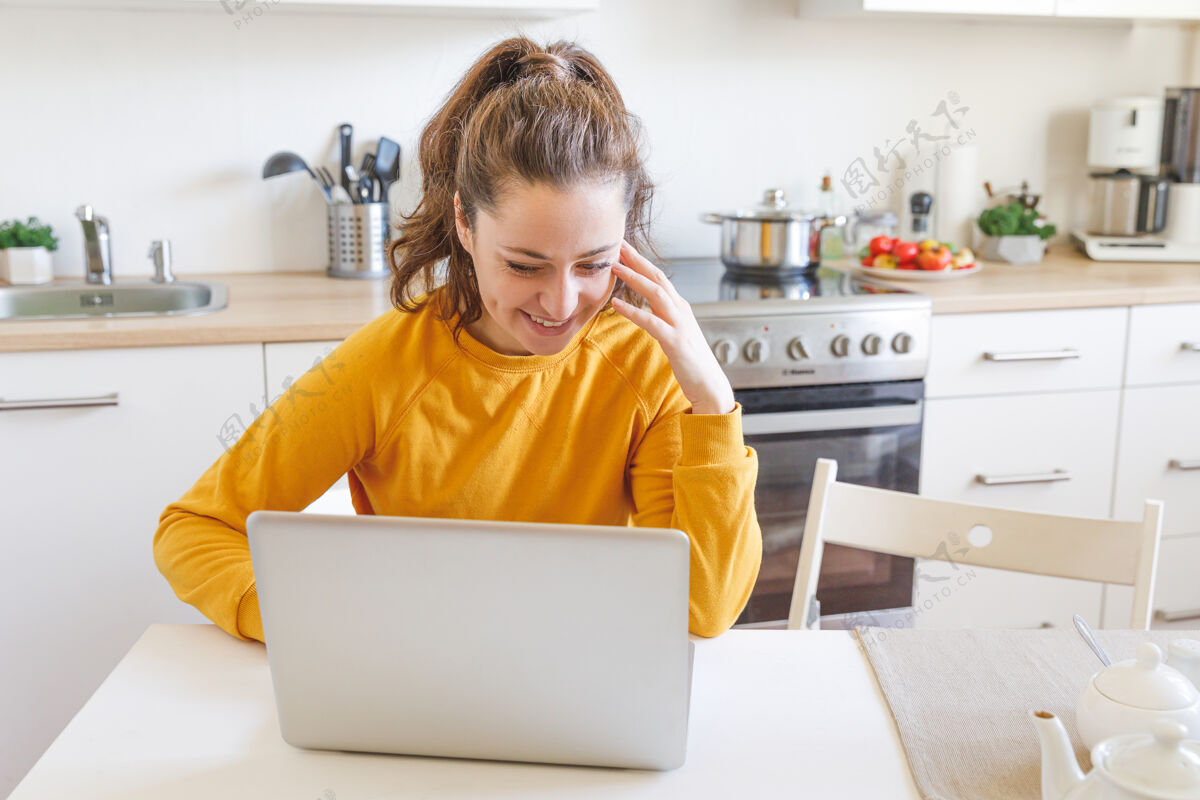 隔离家里有移动办公室年轻女子坐在厨房里用笔记本电脑工作生活方式女孩在室内学习或工作移动设备技术桌子