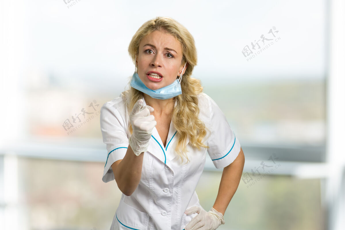工作愤怒的年轻护士用手指指着医院窗户上沮丧的女医生或护士责骂成人保健