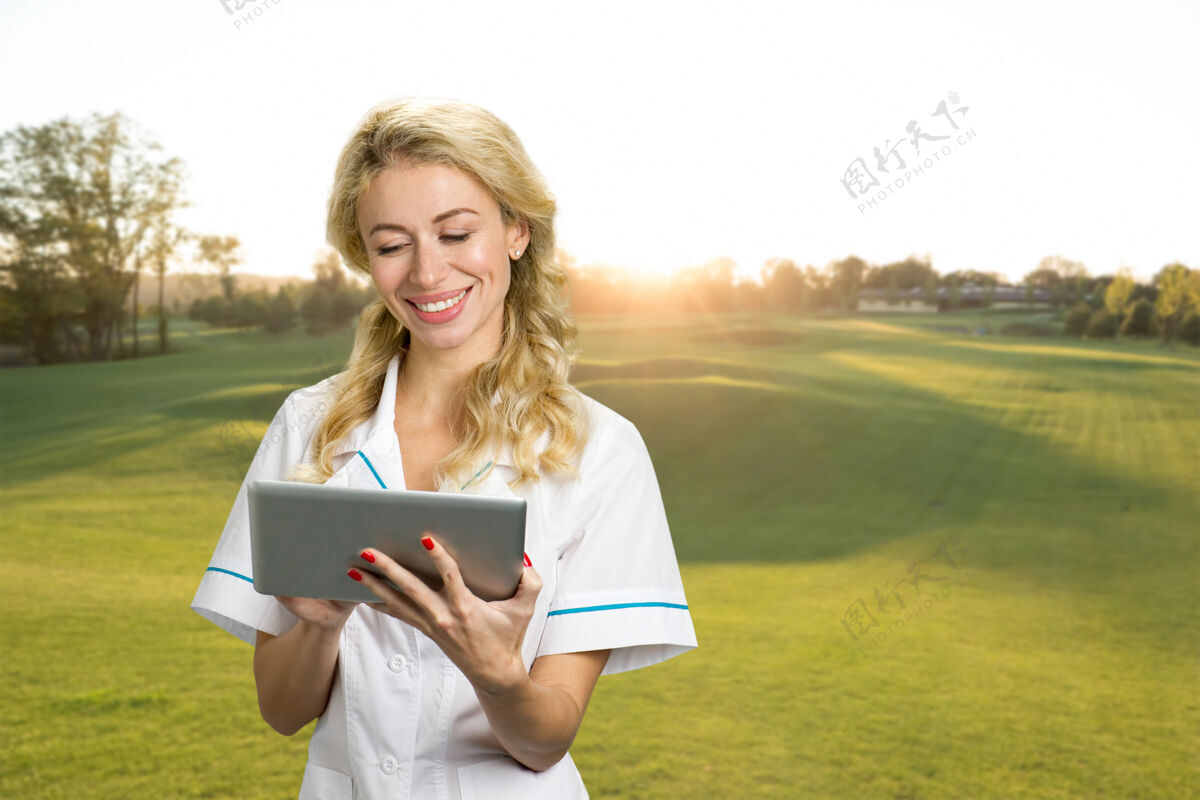 女性美丽的护士在户外使用电脑平板电脑年轻的女医生微笑着在大自然中使用数码平板电脑积极的情绪与户外电子技术外科医生平板电脑专家