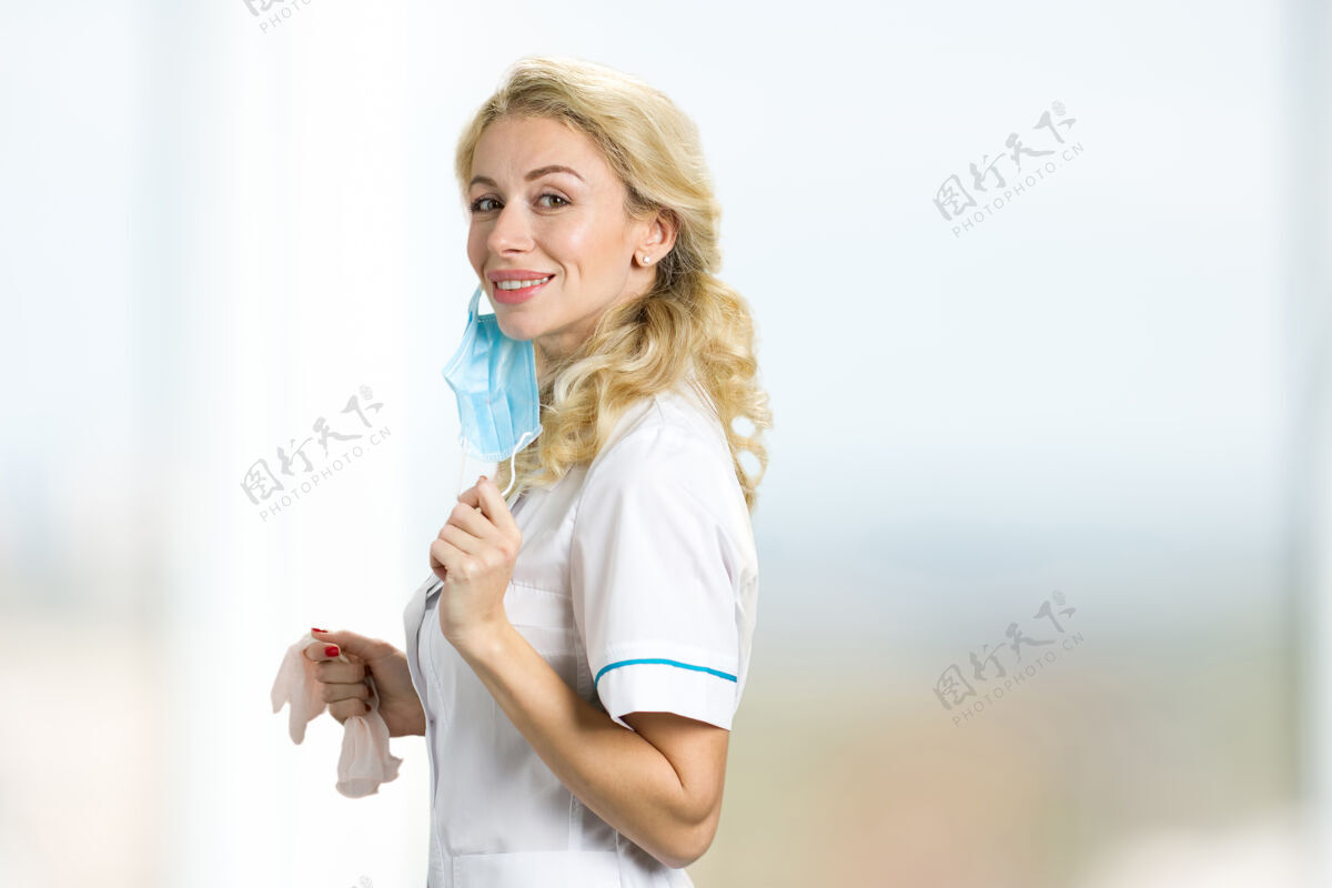 护理微笑的年轻金发护士的肖像美丽的年轻女医生手持面罩和白色乳胶手套 侧视图美丽制服外科医生