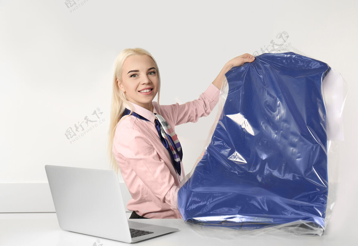 服务女洗衣工在接待处拿着干净的衣服接待衣架笔记本电脑