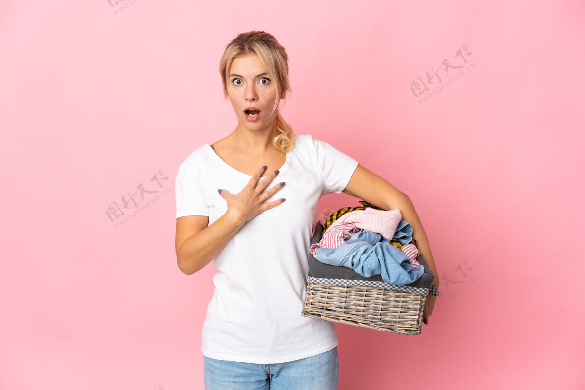 洗衣机年轻的俄罗斯女子拿着一个衣服篮子孤立在粉红色的背景惊讶和震惊 而寻找权利成人年轻广