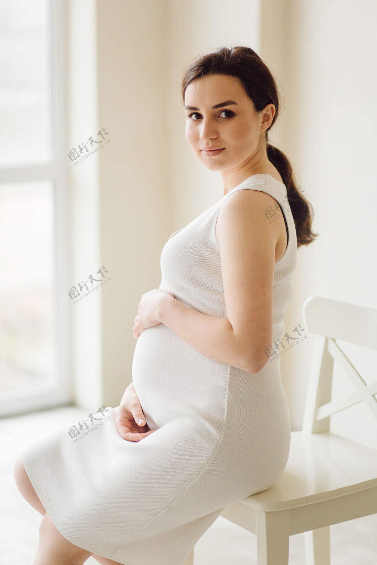 腹部美丽的年轻孕妇穿着礼服在摄影棚摆姿势女性温柔黑发