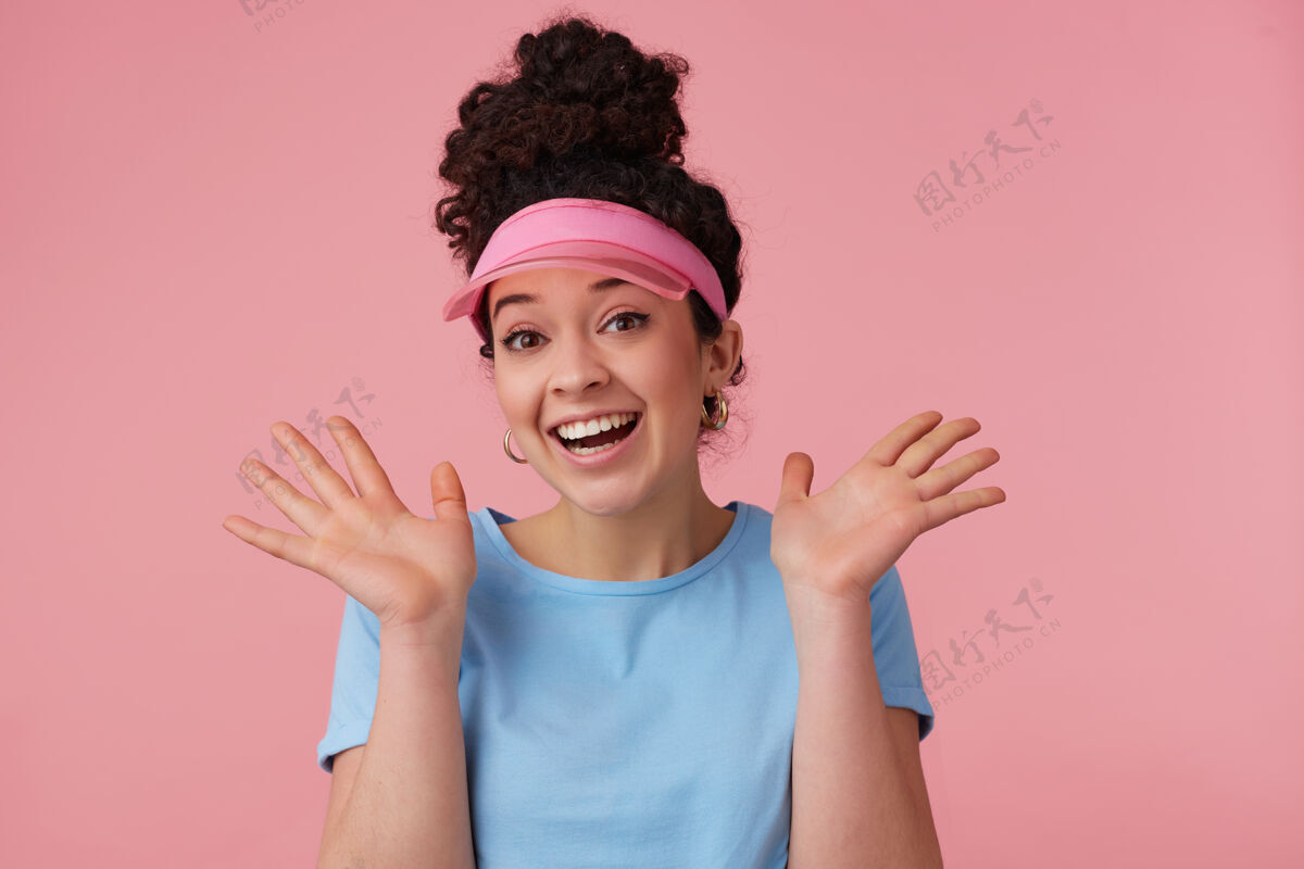 欧洲开朗的女孩 快乐的女人 深色卷发发髻戴着粉红色的面罩 耳环和蓝色的t恤化妆人和情感的概念完美帽舌发髻