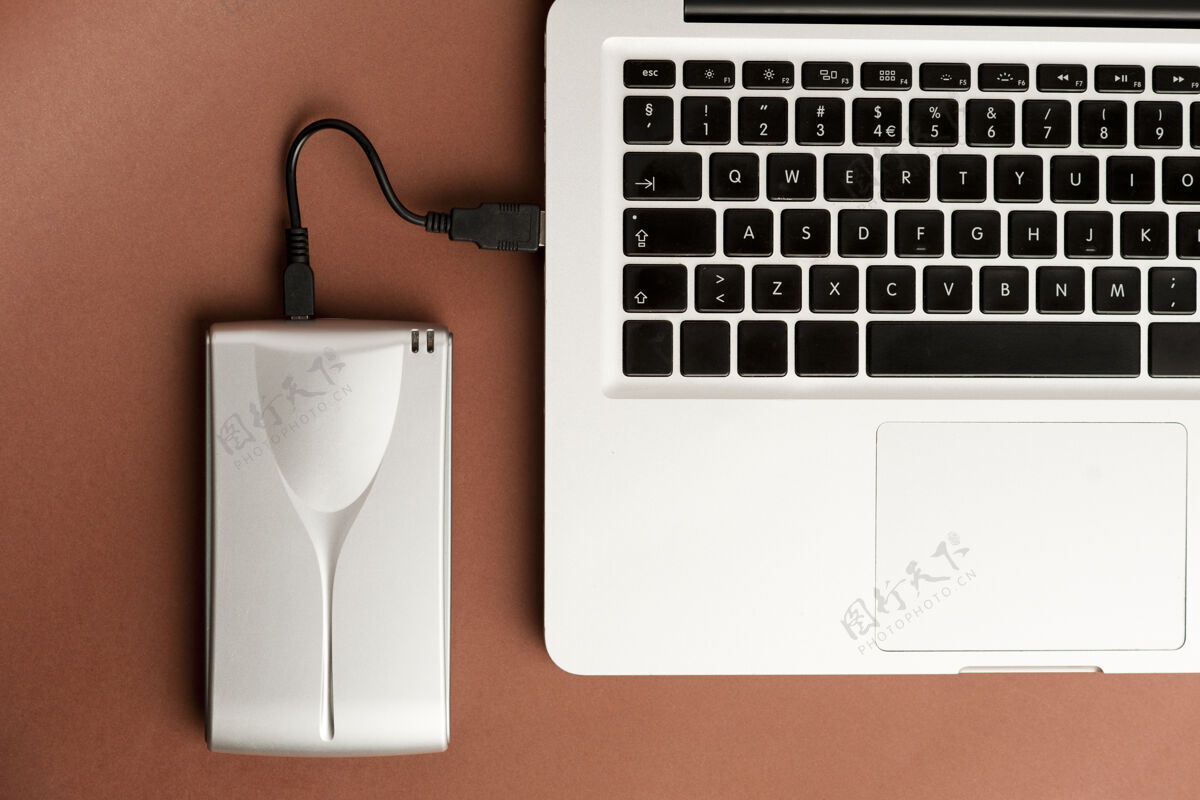 外部铝制外置硬盘 带usb电缆 连接到棕色办公桌面上的笔记本电脑上硬办公桌手机