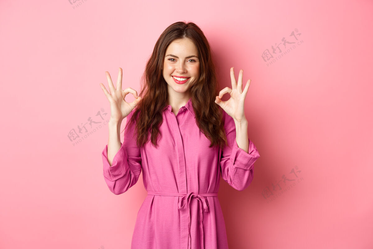 休闲20多岁的美女 喜形于色 满意地点头微笑 满意地站着 站在粉红色的墙上微笑同意时尚